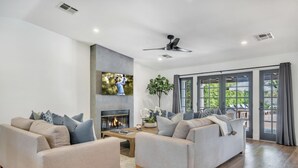 Ein modernes Wohnzimmer mit zwei Sofas, einem Kamin, einem Deckenventilator und einem großen Fenster mit Blick auf Grünflächen.