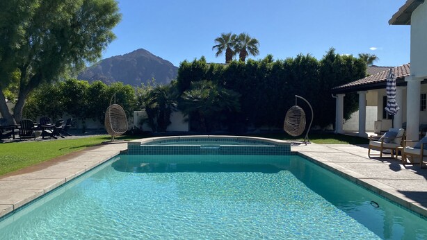Une piscine aux eaux cristallines, avec une vue sur une montagne en arrière-plan, entourée de verdure et de mobilier d’extérieur.