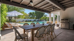 Eine überdachte Terrasse mit Pool, Gartenmöbeln und Grill.