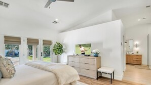 Ein modernes Schlafzimmer mit einem großen Bett, einem Schminktisch, einem Fernseher und Blick ins Freie.