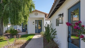 Une maison avec un jardin devant, une porte bleue et un petit potager où poussent différentes plantes et fleurs.