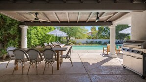 Une terrasse extérieure avec une piscine, un barbecue et une table avec des chaises.