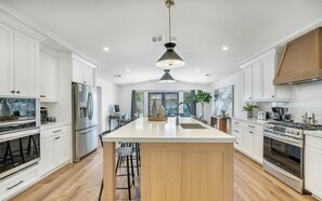 Une cuisine moderne avec des meubles blancs, un îlot central, des appareils en acier inoxydable et un luminaire suspendu.