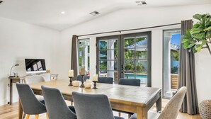 Ein modernes Esszimmer mit einem großen Holztisch, grau gepolsterten Stühlen und einem Flachbildfernseher auf einem Standfuß.