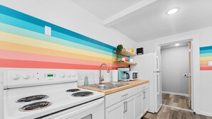 Une cuisine avec des appareils électroménagers blancs, un plan de travail en bois et un mur aux couleurs de l’arc-en-ciel.