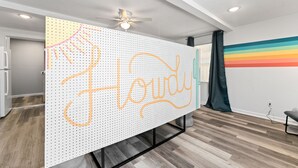 Une pièce avec un mur de séparation blanc sur lequel est inscrit le mot « Houdini » en lettres cursives orange, un ventilateur de plafond et un mur aux couleurs de l’arc-en-ciel.