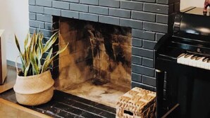 A fireplace with a brick facade, a mirror above it, and a piano to the right. - West Park House | Relaxing Park Life (Chico)