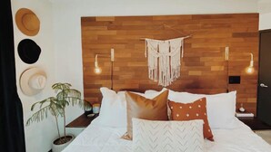 A bedroom with a wooden headboard, a macrame wall hanging, and a bed with white bedding and patterned pillows. - West Park House | Relaxing Park Life (Chico)