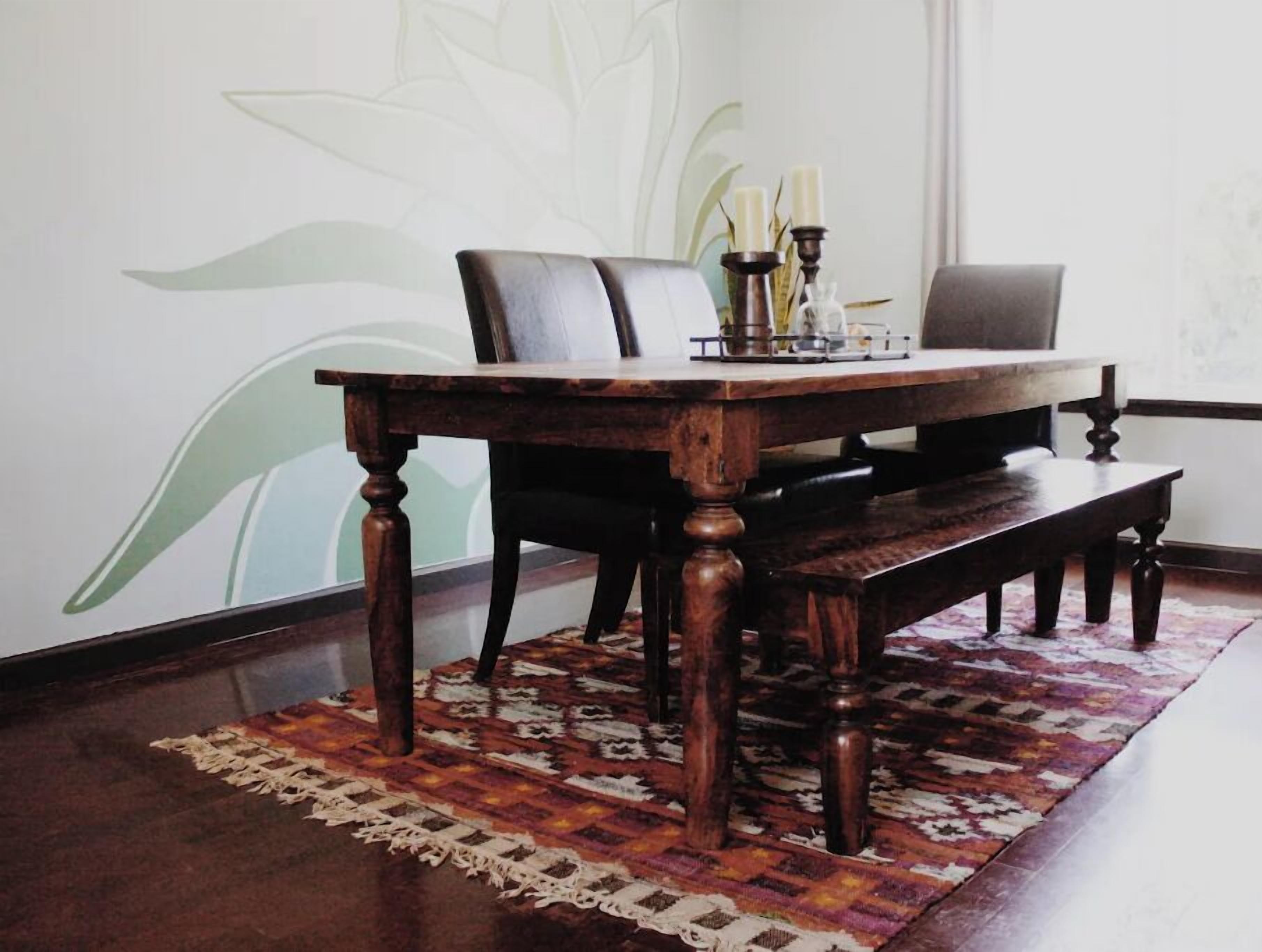 A wooden dining table with a bench, set on a patterned rug, against a wall with a floral design.