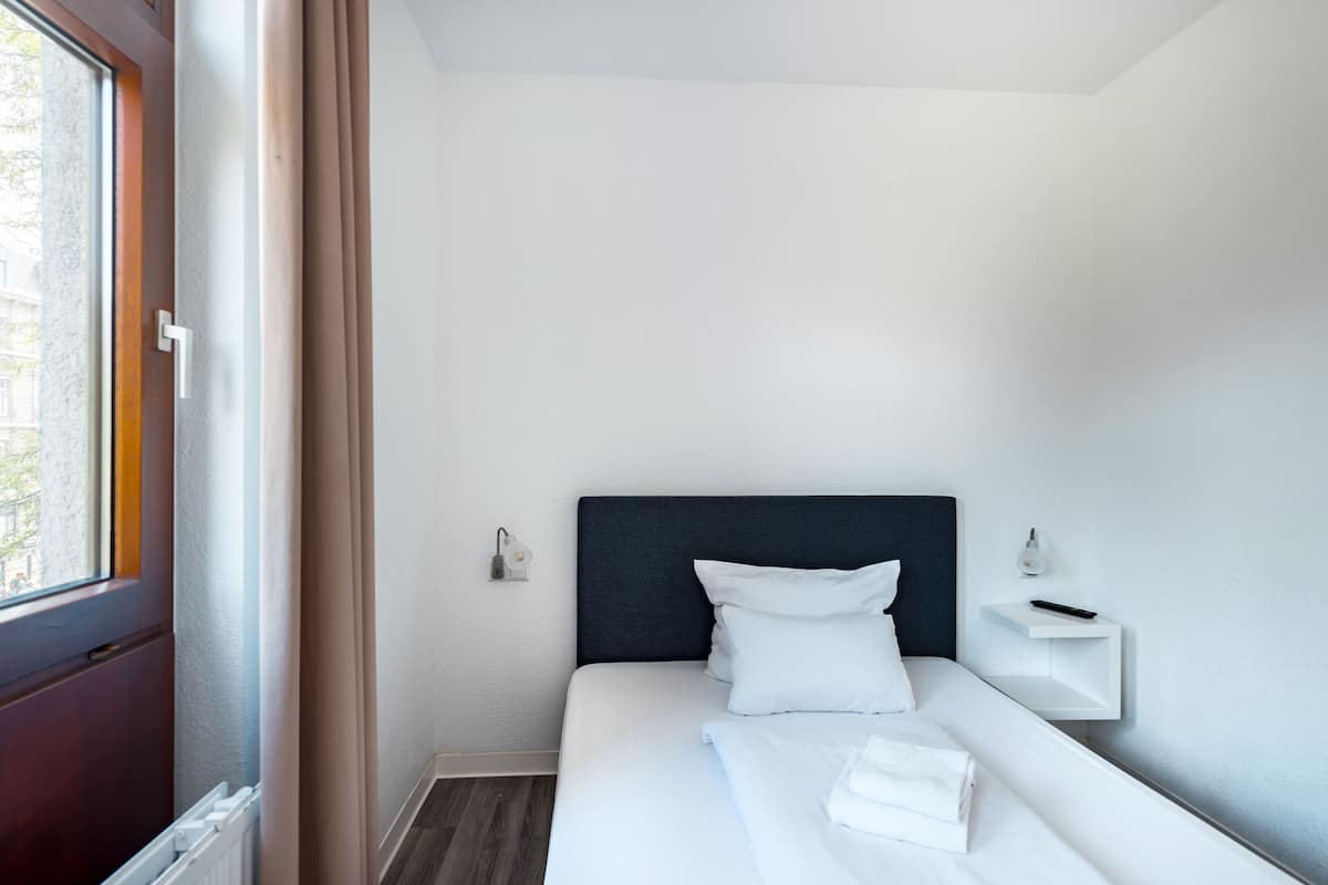 A hotel room with a bed, a bedside table, a nightstand, a window, and a view of the outside.