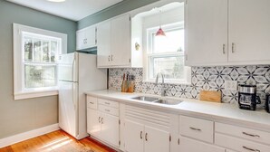 A kitchen with white cabinets, a refrigerator, a sink, and a coffee maker.