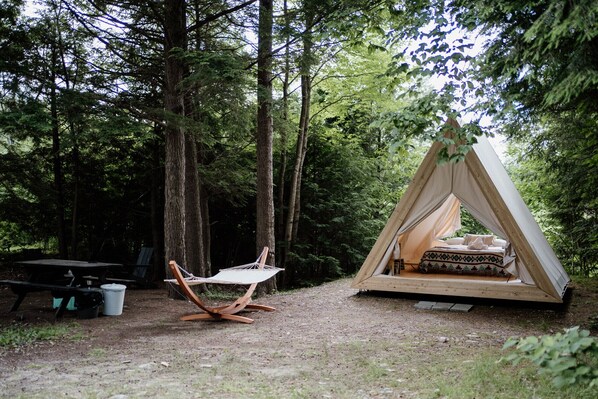 Ein Waldcampingplatz mit Hängematte, Picknicktisch und einem Zelt im Tipi-Stil.