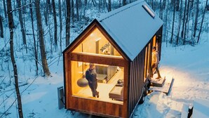 Una baita di legno con facciata in vetro, un letto e un angolo cottura.