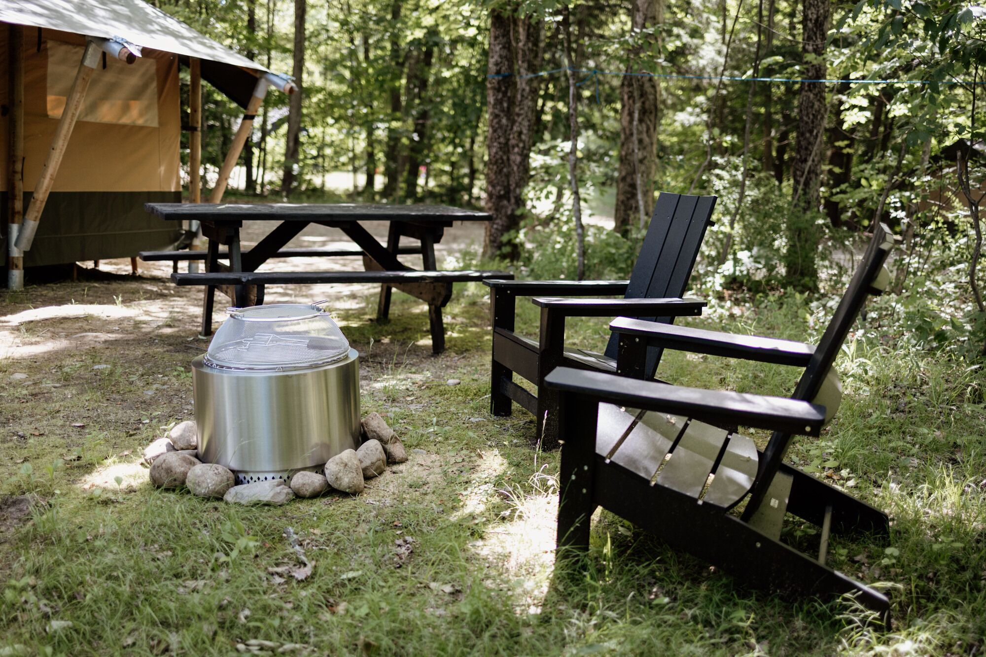 A campsite with a metal grill, picnic table, and a chair.