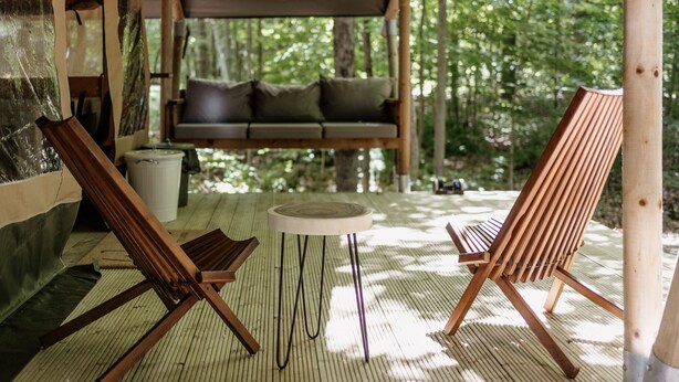 Una terraza de madera con dos sillones de descanso y una mesita, rodeada por un tapete de bambú.