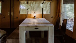 A small, cozy room with a wooden table and a single chair, a lantern on the table, and a window with a view of trees.