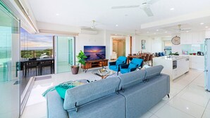 A modern living room with a grey sofa, blue armchairs, a TV, and a balcony with a view.