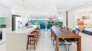 A modern kitchen with a central island, dining area with wooden chairs, and a large window offering a view.
