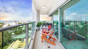 A balcony with a view of the city, a table with chairs, and a potted plant.