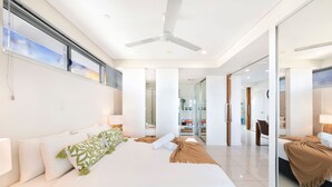 A modern hotel room with a large bed, a ceiling fan, and a glass door leading to a bathroom.