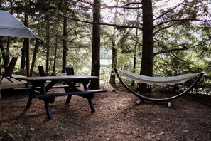 Un montaje para picnic con mesa y bancos, una hamaca y una tienda de campaña en un área boscosa.