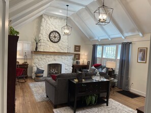 A spacious living room with a stone fireplace, a large clock, and a high ceiling with exposed beams. - Great for parent weekends and orientation (Athens)