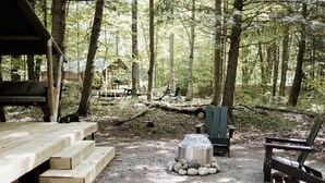 Un área de estar al aire libre de estilo rústico con bancos de madera y una mesa de metal, rodeada de árboles en un entorno boscoso.