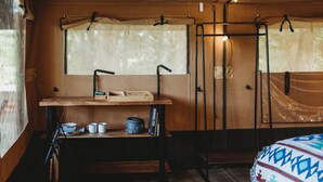 A compact, well-organized room with a wooden table, a hanging rack, and a bed with a patterned blanket.