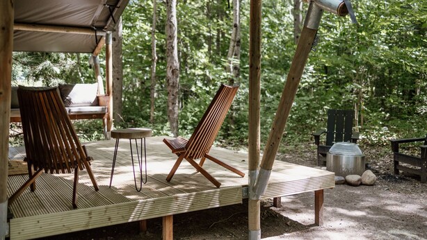 A wooden deck with a swing chair and a cushioned chair, surrounded by a forest.