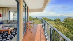 A balcony with a view of the sea, a sofa, a table, and a chair inside a room. - ZEN88 Esp (408): Coastal Elegance ~ Sunset ~ Pool (Darwin City)