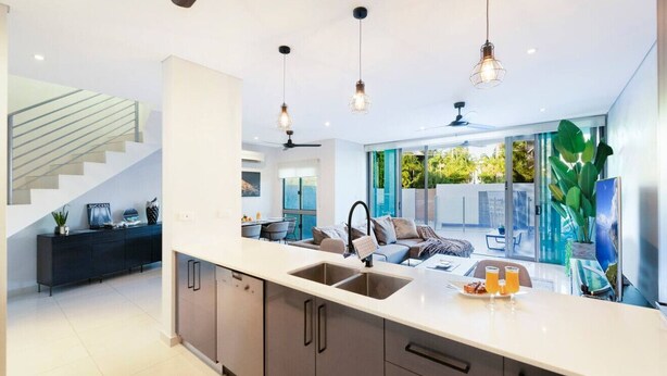 Una cocina moderna con una isla central, electrodomésticos integrados e iluminación colgante.