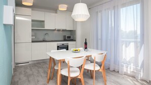 Una cocina moderna con armarios blancos, microondas y un comedor con mesa y sillas blancas.