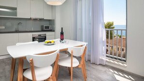 Una cocina moderna con armarios blancos, una mesa de comedor con sillas y vistas al mar a través de un amplio ventanal.