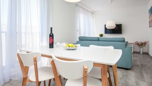 Un salón moderno con una mesa de comedor blanca, sillas de madera, un sofá color turquesa y un televisor de pantalla plana montado en la pared.