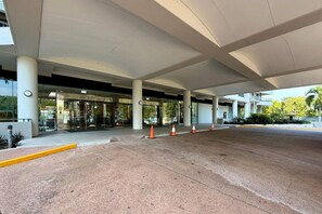 A modern building entrance with a covered walkway, glass doors, and a paved area with traffic cones. - Coastal Splendor: Seaview ~ Pool ~ Balcony Dining (Darwin City)