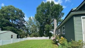 Une maison d’habitation avec une pelouse bien entretenue, une clôture en bois peinte en blanc et une cheminée en briques.