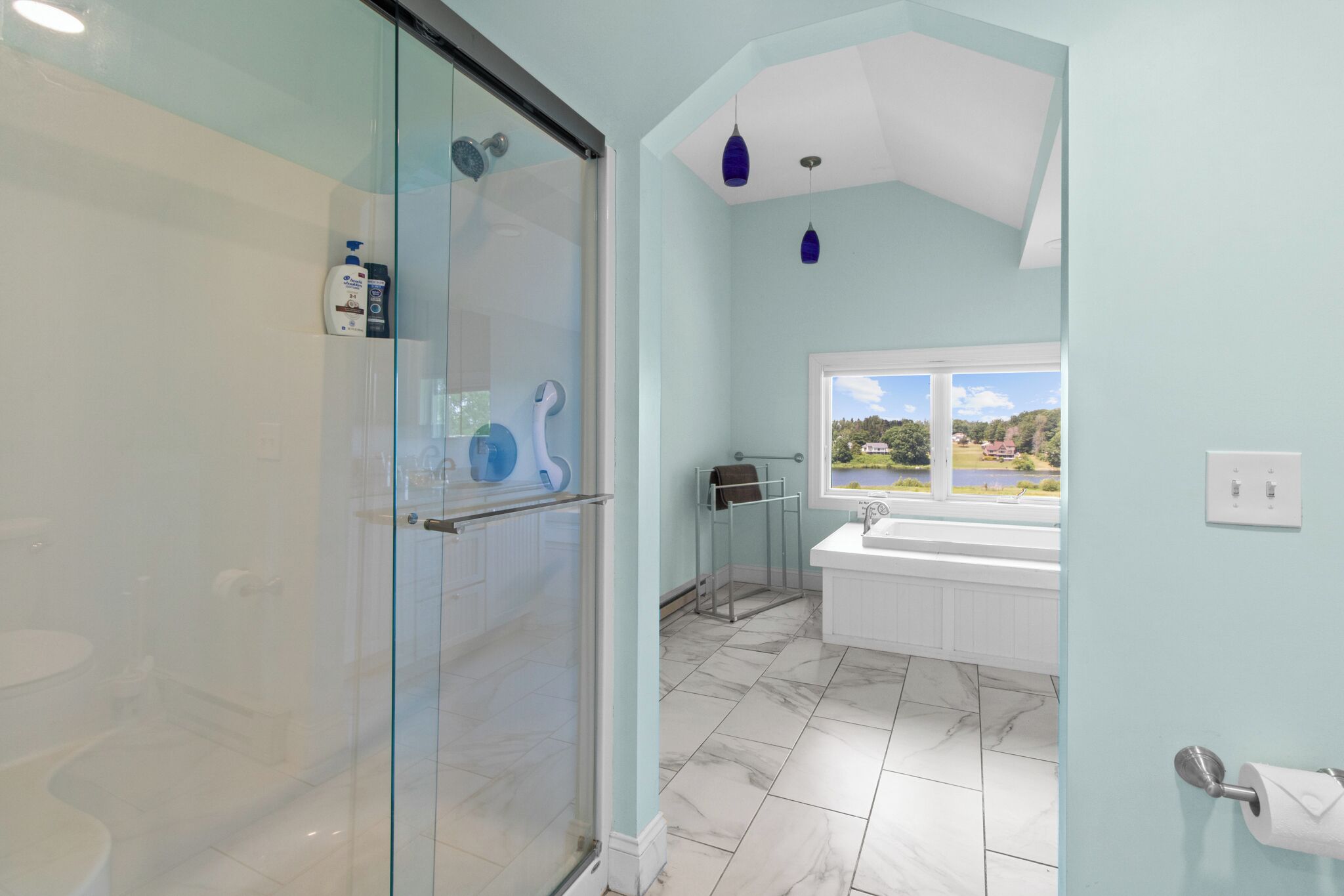 Ein Badezimmer mit Duschkabine aus Glas, einer weißen Badewanne, einem Fenster mit Aussicht und einem Marmorboden.