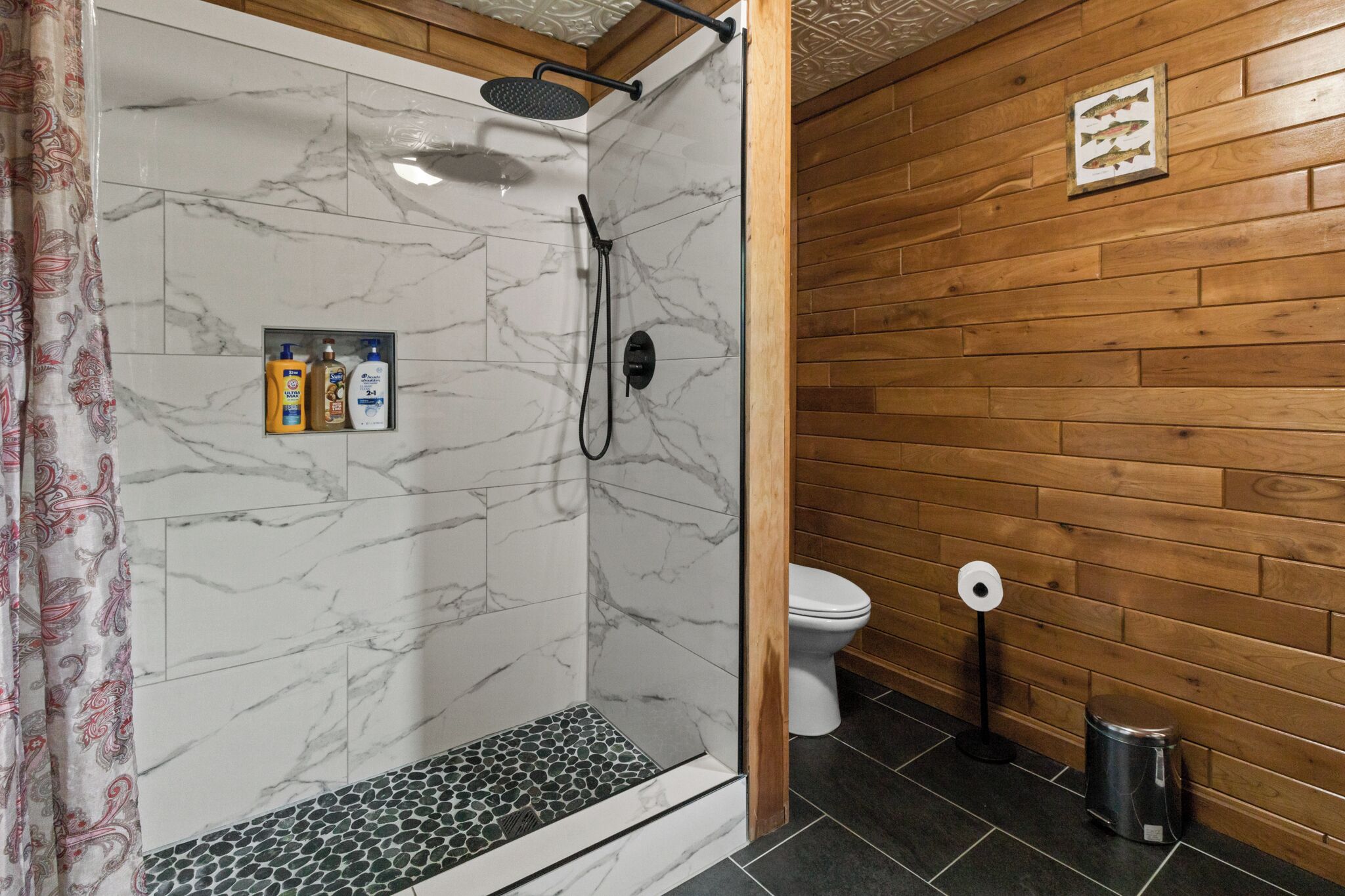 Baño con ducha, inodoro y un pequeño cubo de basura.