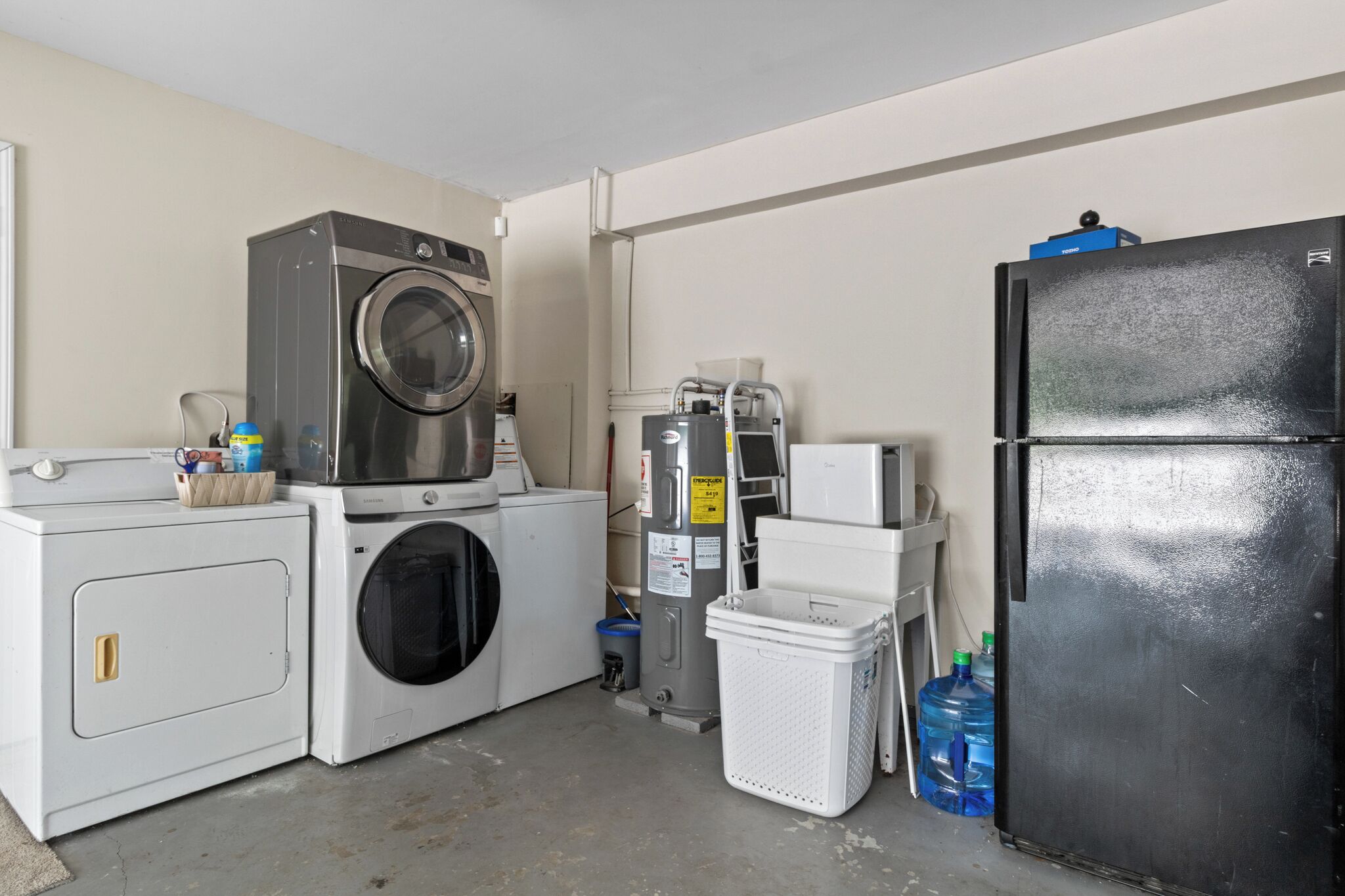 Ein Waschraum mit Waschmaschine, Trockner, Kühlschrank und Wasserspender.