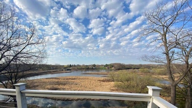 Une vue sur le fleuve depuis une terrasse dotée d’une balustrade, un ciel dégagé et un paysage lointain comprenant des arbres et des bâtiments.