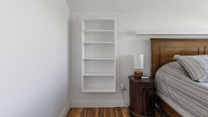 Une chambre à coucher avec un lit, une table de chevet, une étagère fixée au mur et un plancher en bois.