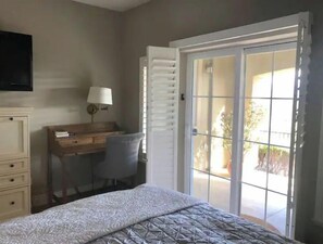 Relax in a cozy space with a comfortable bed, desk, and TV, plus a sliding door leading to an outdoor area.