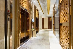 Un couloir d’hôtel avec un ascenseur, un comptoir de réception et un mur orné de motifs.