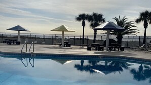 A swimming pool with lounge chairs and umbrellas, surrounded by palm trees and a fence. - Family Friendly Venture Out Getaway  (Panama City Beach)