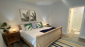 A bedroom with a wooden bed, two bedside tables, a nightstand, a striped rug, and a door leading to a bathroom. - Family Friendly Venture Out Getaway  (Panama City Beach)