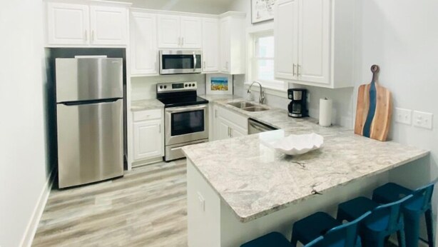 A modern kitchen with white cabinets, stainless steel appliances, a marble island with bar stools, and a wooden guitar on the wall. - Family Friendly Venture Out Getaway  (Panama City Beach)
