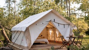 Una carpa con una cama, una mesa y sillas en su interior, rodeada de árboles.