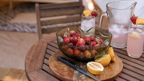 Una mesa de comedor con un cuenco de fresas, un cuchillo y una jarrón de limonada en una carpa.