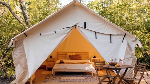 Una carpa con una cama, una mesa y sillas instaladas en un bosque.