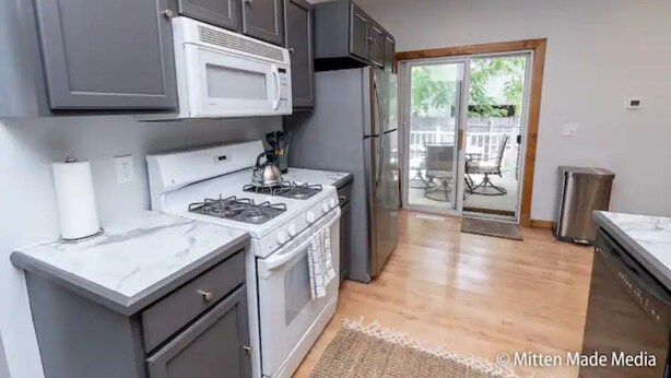 A modern kitchen with grey cabinets, a white stove, and a stainless steel refrigerator.